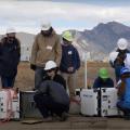 Scientists in white hardhats stand outside examining white boxes containing scientific equipment